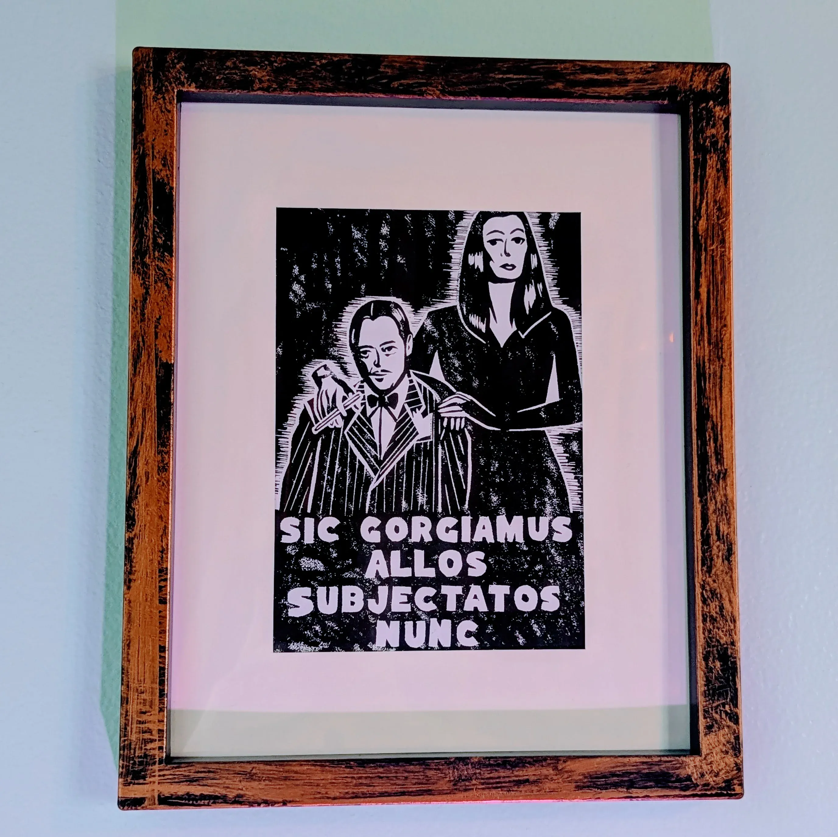 a linocut print in black and white framed. the linocut is of the addams family and reads 'sic gorgiamus allos subjectatos nunc'